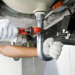 Technician plumber using a wrench to repair a water pipe under the sink. Concept of maintenance, fix water plumbing leaks, replace the kitchen sink drain, cleaning clogged pipes is dirty or rusty.